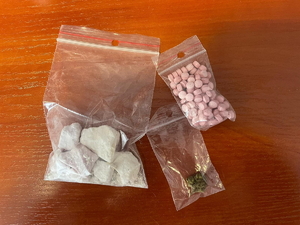 zdjęcie kolorowe - na biurku leżą trzy woreczki, w jednym biała zbrylona substancja, w drugim zielony susz, a w trzecim różowe tabletki
