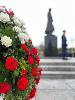 Wiązanka kwiatów przy pomniku, w tle policjanci w mundurach galowych