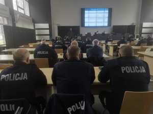 Policjanci w mundurach służbowych siedzą w ławkach skierowani w stronę mównicy i słuchają wykładu