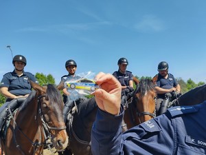 Policjanci na koniach stoją przy ogrodzeniu za którym stoją dzieci
