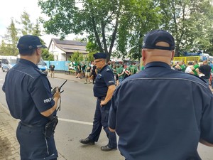 Policjanci patrolują rejon bramy stadionu przy której stoi grupa kibiców
