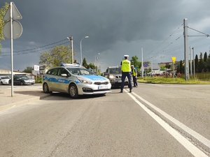 Policjant stoi przy radiowozie i blokuje ruch uliczny