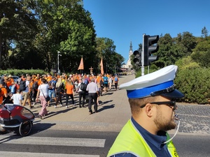 Policjant stoi na drodze, przez która przechodzą pielgrzymi