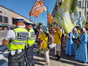 Policjanci stoją z pielgrzymami i oczekują na przejście przez jezdnię