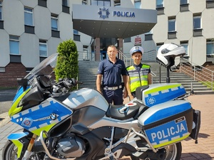 Policjant z chłopcem w stroju policjanta pozuje do zdjęcia na tle komendy przy motocyklu