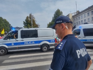 Policyjne radiowozy na drodze, obok przechodzi policjant