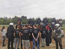 Młodzież stoi zwrócona w kierunku policjantów siedzących na koniach