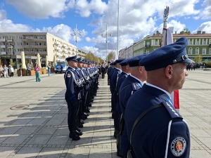 Policjanci w umundurowaniu wyjściowym stoją  w dwuszeregu na placu