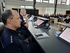 Policjanci siedzą przy ławie i słuchają wykładu