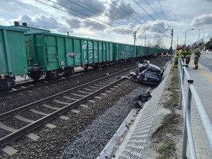 Zniszczony pojazd przy torowisku na którym stoją wagony pociągu