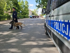 Przewodnik z psem służbowym przechodzi przez drogę w okolicy radiowozu