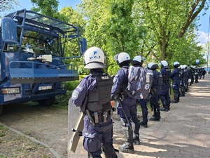 Policjanci stoją przy armatce wodnej i zabezpieczają miejsce