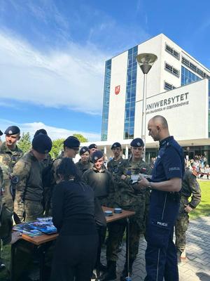 Policjant rozmawia z młodzieżą przy stoisku profilaktycznym