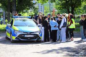 Młodzież rozmawia z policjantem, który stoi przy radiowozie