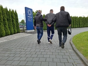 Policjanci nieumundurowani doprowadzają zatrzymanego przy tablicy z napisem Komenda Miejska Policji w Częstochowie