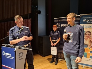 Policjant i policjantka rozmawiają z młodym mężczyzna na scenie