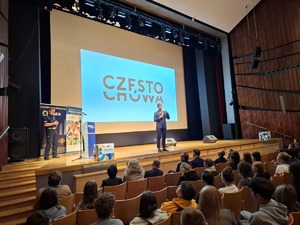 Mężczyzna ze sceny przemawia do słuchaczy w tle na ekranie wyświetla się napis Częstochowa
