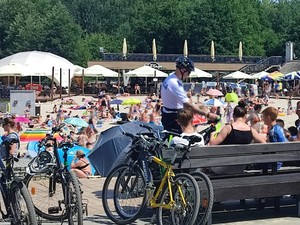 Policjant wśród wypoczywających w parku turystów wręczają im opaski odblaskowe