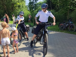 Policjant na rowerze wręcza opaski odblaskowe dzieciom