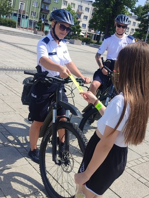 Policjanci na rowerach podczas patrolu wręczają opaskę odblaskową dziewczynce