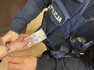 Policjant spina kajdankami ręce, które trzymają banknot