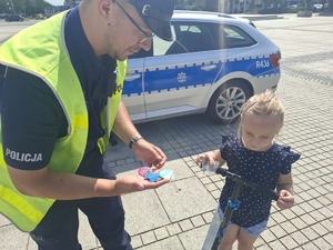 Policjant wręcza element odblaskowy dziewczynce na hulajnodze