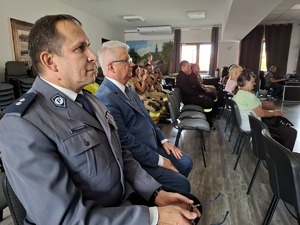 Policjant i burmistrz siedzą na krzesłach w sali widowiskowej wśród strażaków