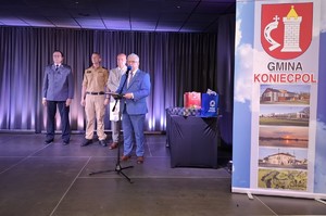 Na scenie burmistrz składa gratulacje chłopcu w towarzystwie strażaków i policjanta