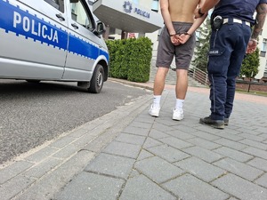 Policjant przy radiowozie stoi z zatrzymanym
