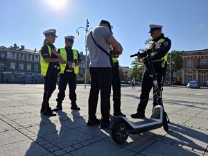 Policjanci rozmawiają z mężczyzną stojącym przy hulajnodze elektrycznej