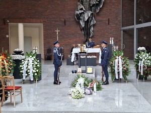 Policjant przemawia z ołtarza pod którym stoi dwóch policjantów przy urnie z prochami