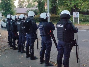 Policjanci uzbrojeni w policyjny sprzęt, stoją przy drodze