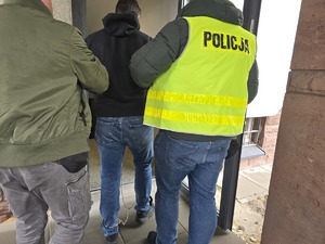 Policjanci doprowadzają zatrzymanego, wchodzą do budynku