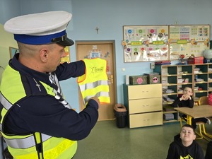Policjant prezentuje dzieciom kamizelkę odblaskową