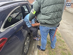 Zatrzymany wysiada z radiowozu w obecności nieumundurowanego policjanta