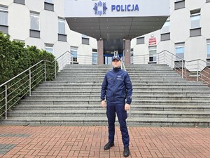 Policjant w umundurowaniu służbowym stoi przed budynkiem komendy