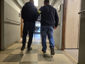 Policjant doprowadza zatrzymanego korytarzem