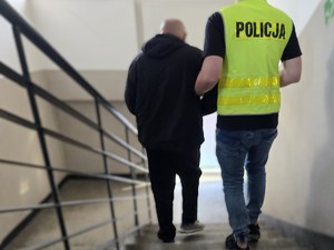 Policjant doprowadza zatrzymanego poi schodach