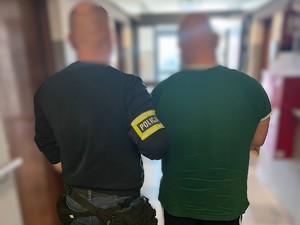 Policjant doprowadza zatrzymanego korytarzem