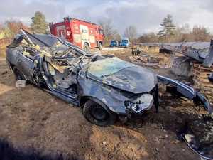 Miejsce zdarzenia, zniszczony pojazd , w tle wóz strażacki i policyjny radiowóz