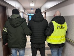 Policjanci doprowadzają korytarzem zatrzymanego