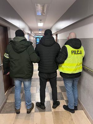 Policjanci doprowadzają korytarzem zatrzymanego mężczyznę