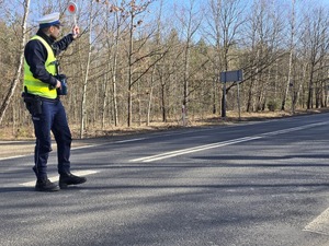 Policjant na drodze unosi tarczę do zatrzymywania pojazdów do góry