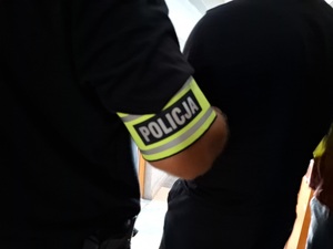 Opaska z napisem Policja na przedramieniu policjanta, który doprowadza zatrzymanego