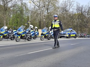 Policjant kieruje ruchem na drodze, w tle motocykliści stoją na drodze
