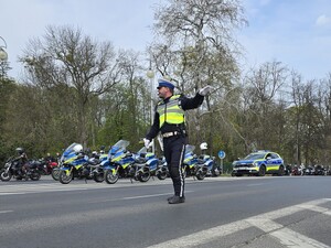 Policjant kieruje ruchem na drodze, w tle stoją motocykliści