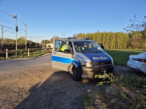 Policjant stoi przy radiowozie na miejscu zdarzenia przy przejeździe kolejowym