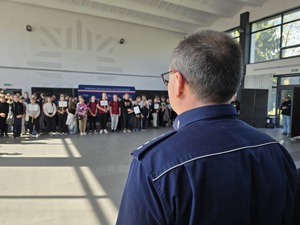 Komendant w mundurze stoi naprzeciwko młodzieży zgromadzonej w auli komendy