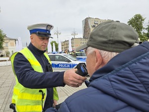 Mężczyzna dmucha w urządzenie do badani stanu trzeźwości, które trzyma policjant