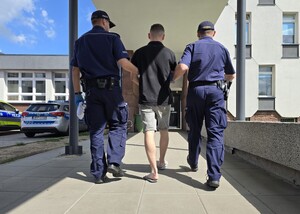 Policjanci doprowadzają zatrzymanego w kajdankach